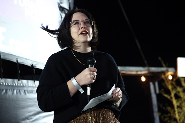 Kayla Gagnet speaking into a microphone onstage at an evening event, holding notes.